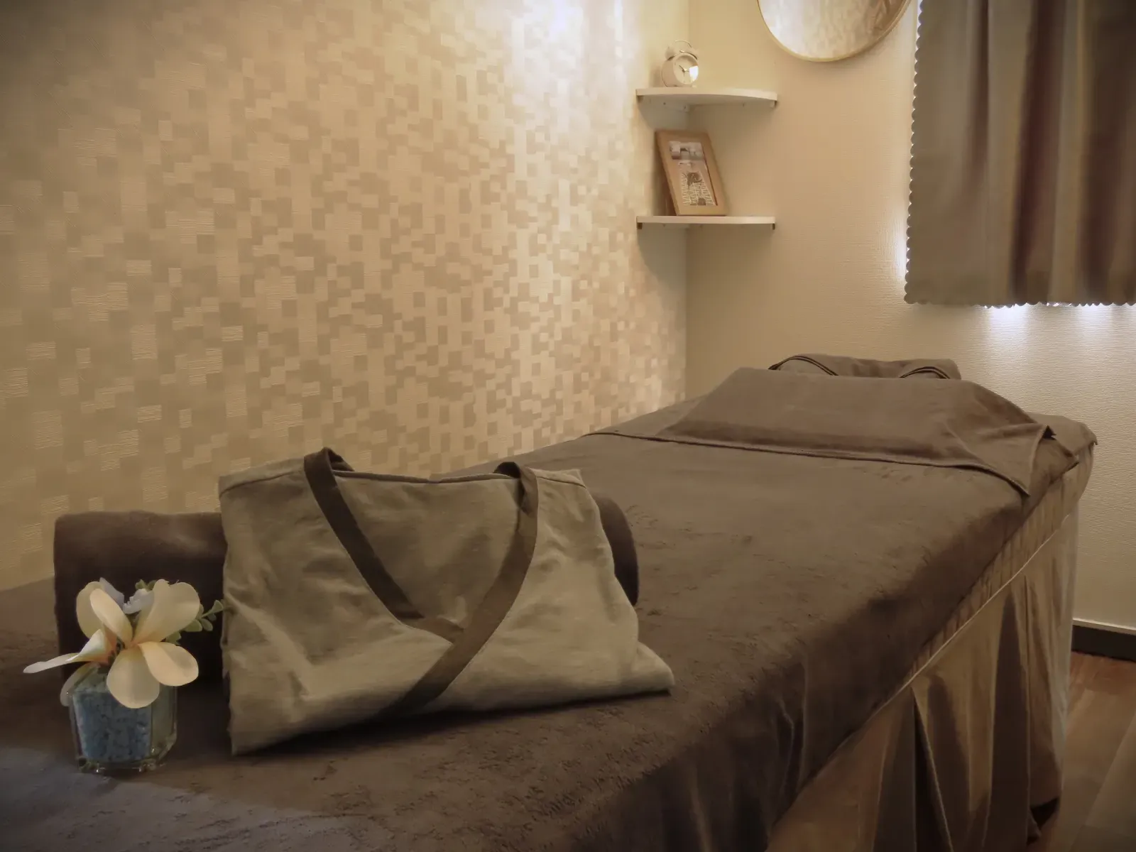 A towel-covered bed with a white flower beside the pillow