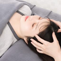 Hands resting on the head of a guest lying face up, a towel around the neck
